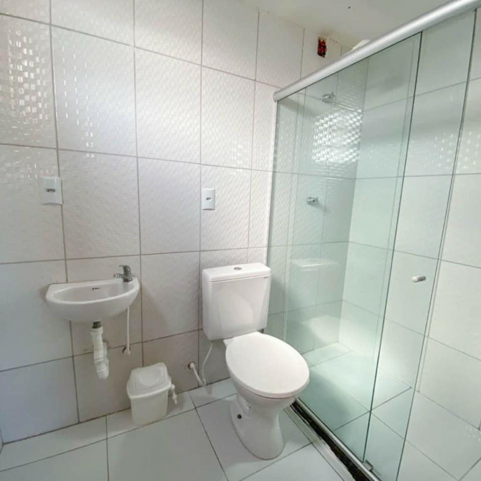 Banheiro com box de vidro e revestimento branco